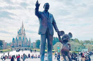 ウォルト・ディズニーとミッキーマウスの像、背後に城と訪問客がいます。