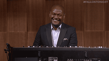 Man in a suit smiling while playing an electronic keyboard