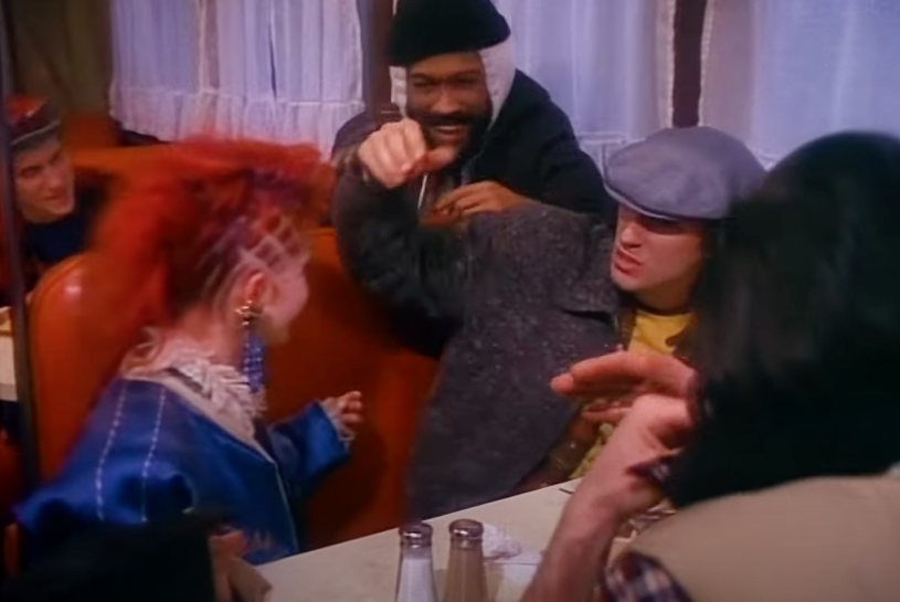 A group of people in a diner, one gesturing dramatically, engaged in an animated discussion