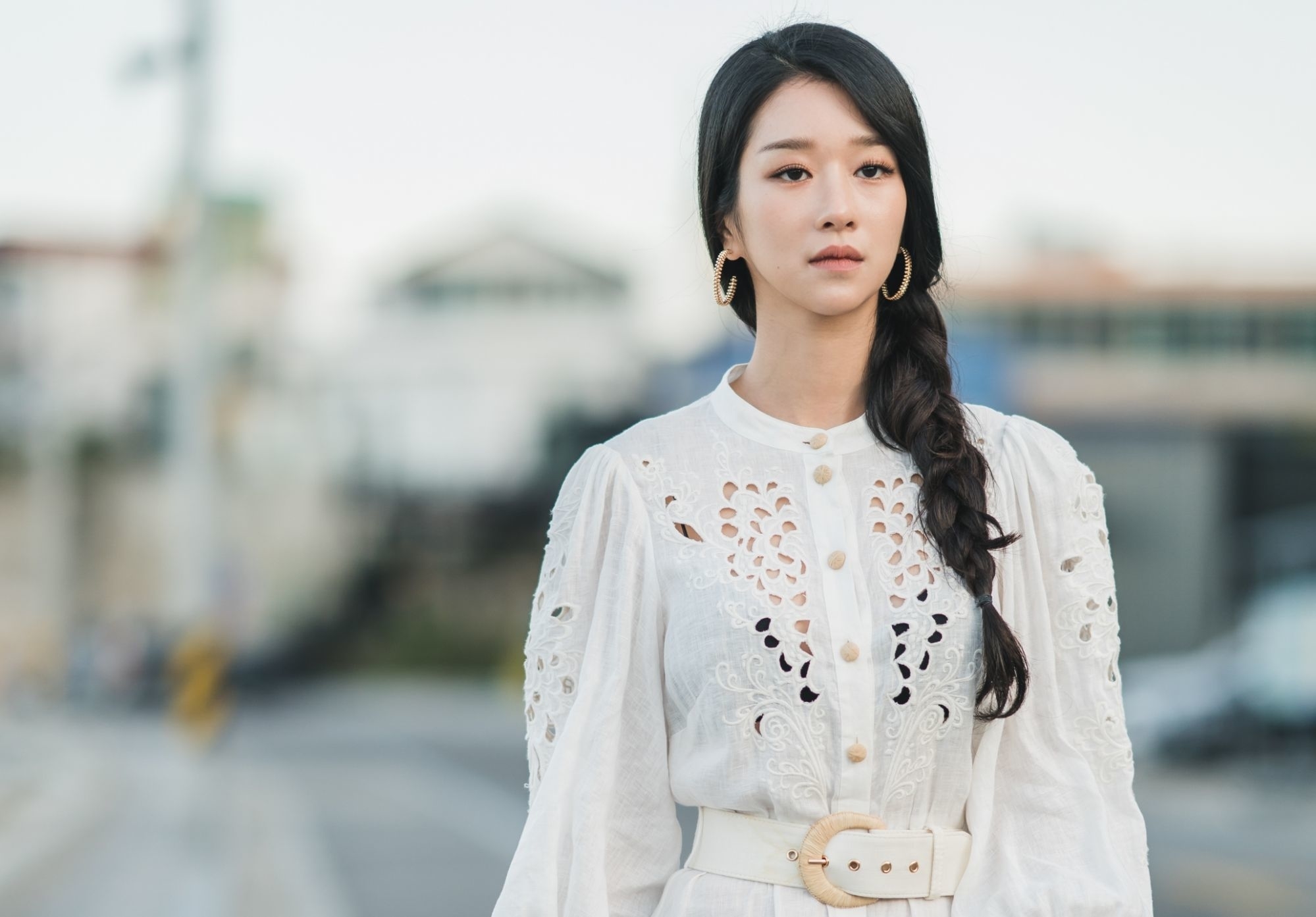 Ko Mun-Yeon, personaje principal de Está bien no estar bien usando un vestido blanco con detalles recortados y un cinturón, de fondo una calle borrosa.