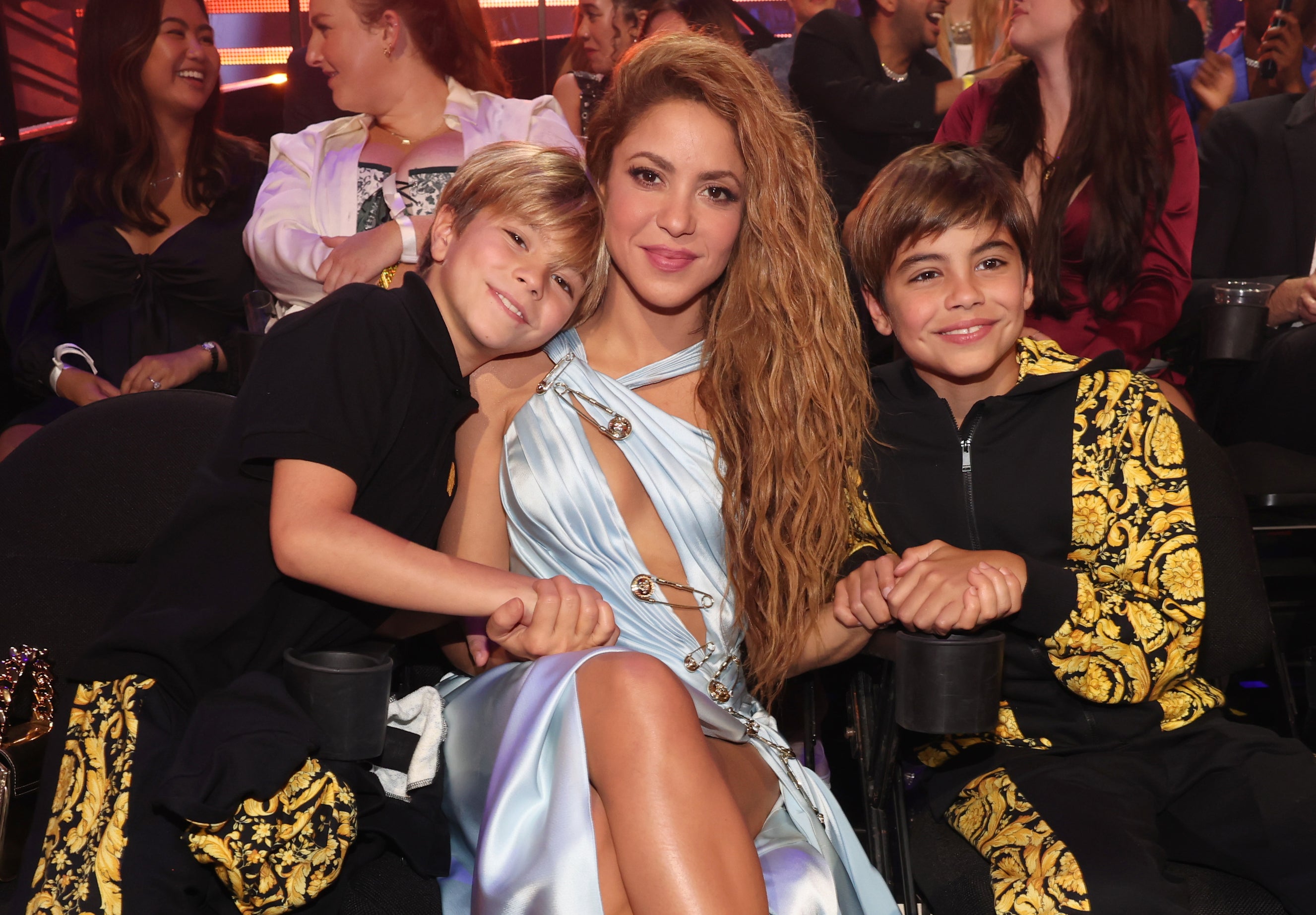 Shakira in a satin dress with a thigh-high slit, seated with her two sons at an awards show