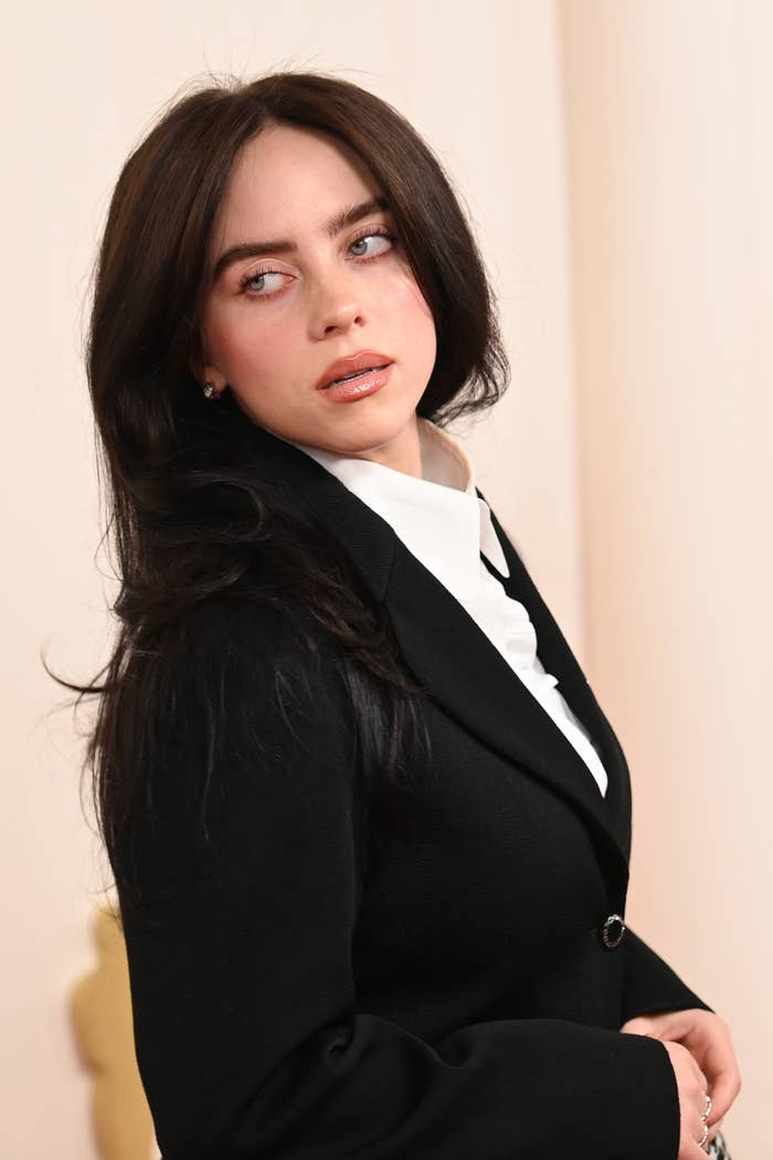 Woman in a black blazer and white shirt posing with a slight turn, looking away from the camera