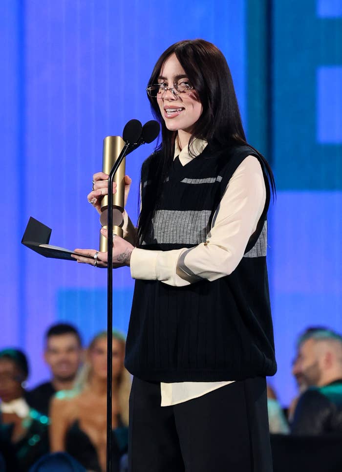 Woman in vest and shirt at a microphone with award, on stage