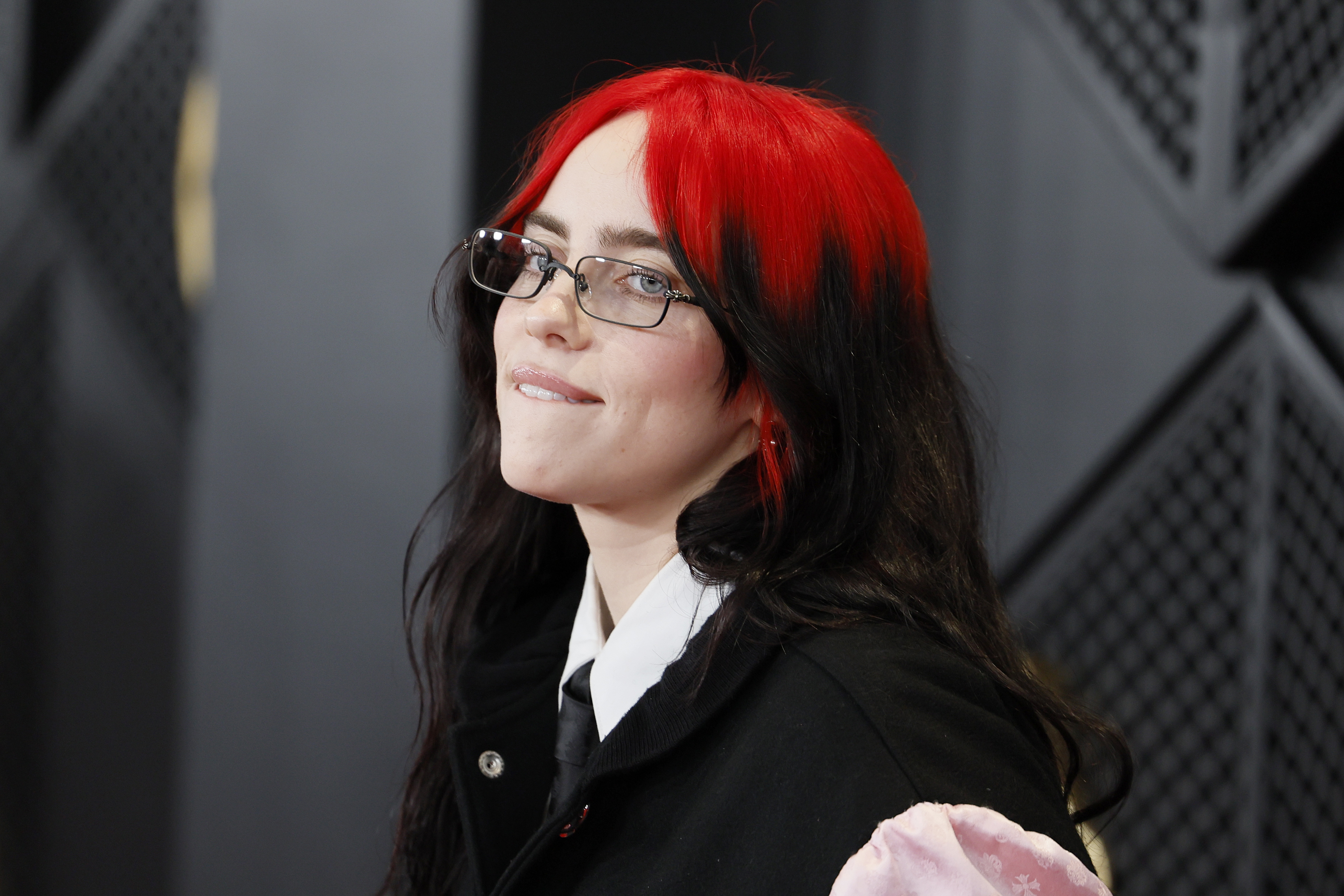 Person with red hair and glasses smiling, wearing a black top and white shirt underneath
