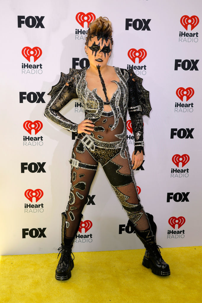 Person in avant-garde outfit with spikes and sheer elements, striking a pose on event backdrop