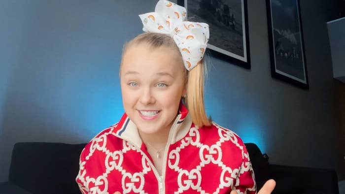 JoJo Siwa smiling in a red Gucci tracksuit with a large bow in her hair