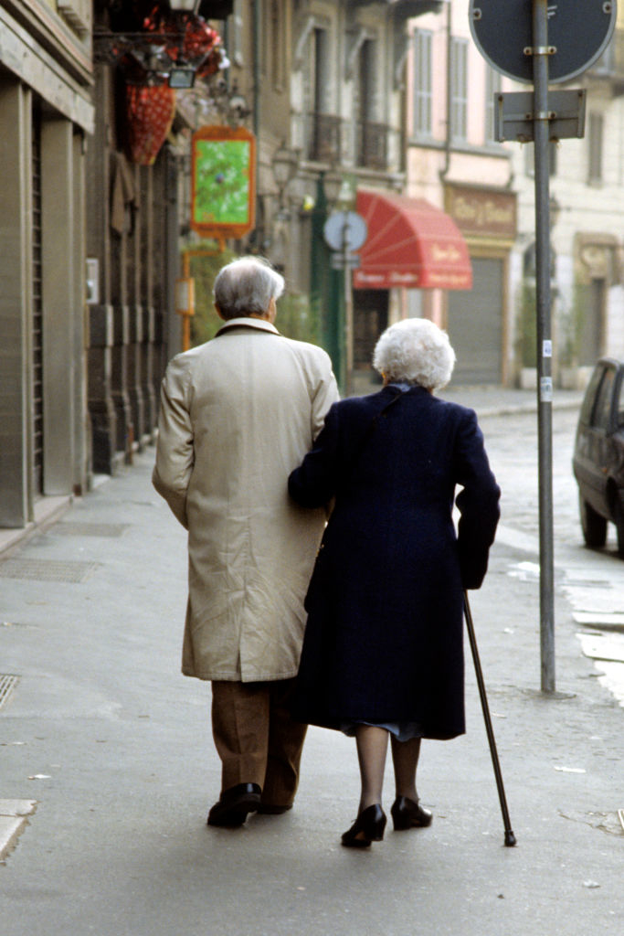 Elderly couple walking arm in arm down a city street, one using a cane