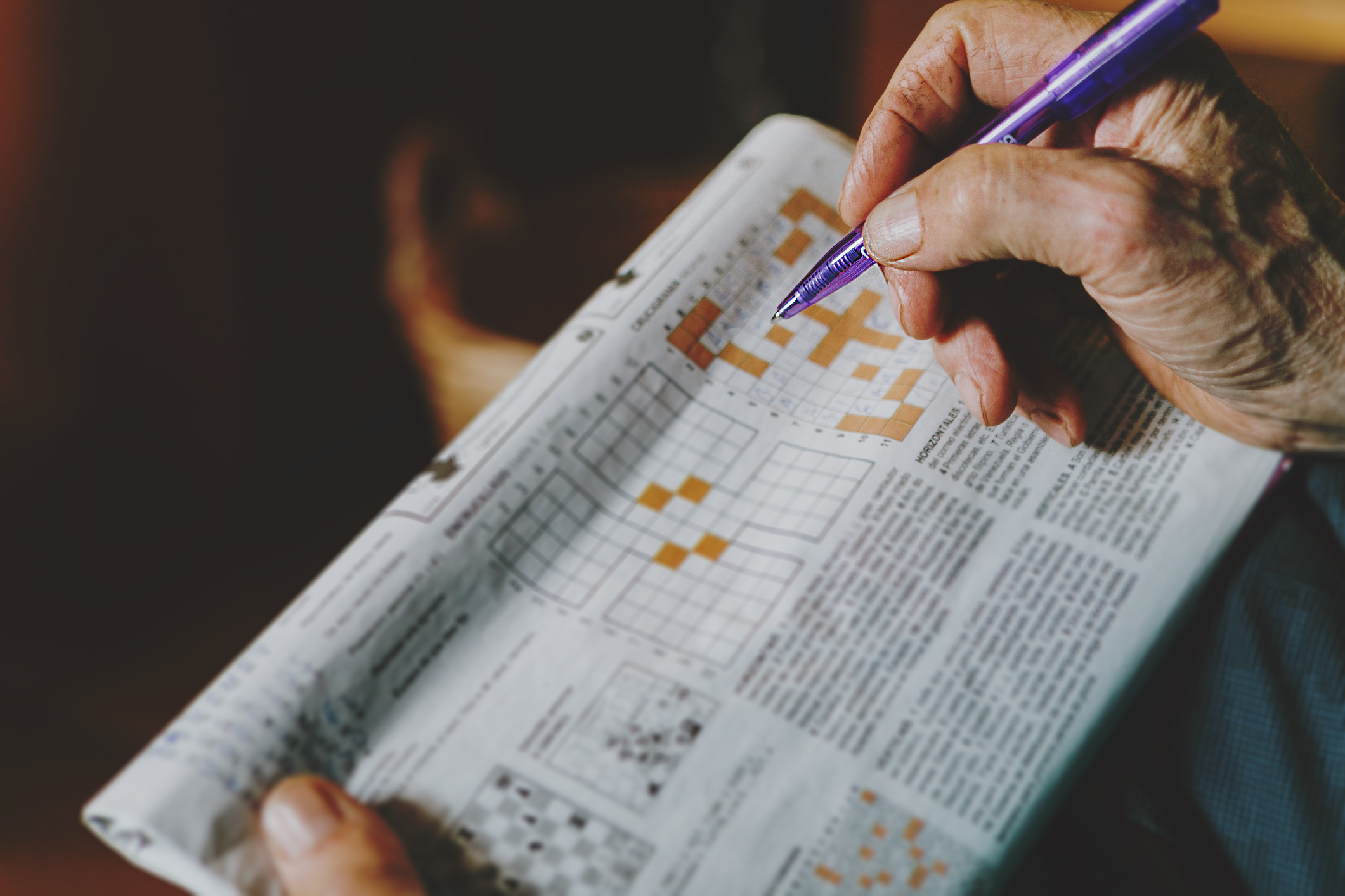 Elderly person&#x27;s hand completing a crossword puzzle in a newspaper