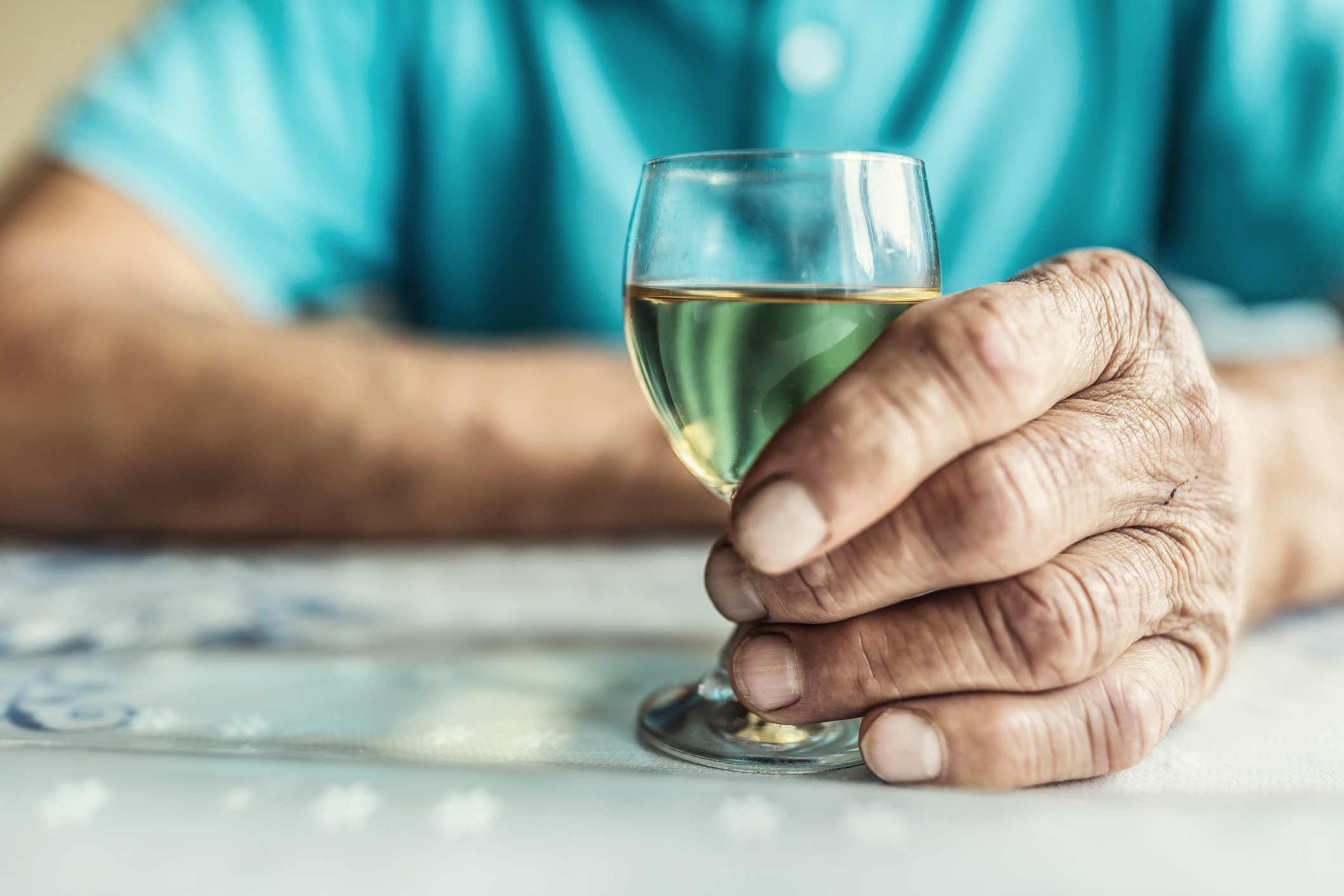 Close-up of an older person&#x27;s hand holding a glass of white wine