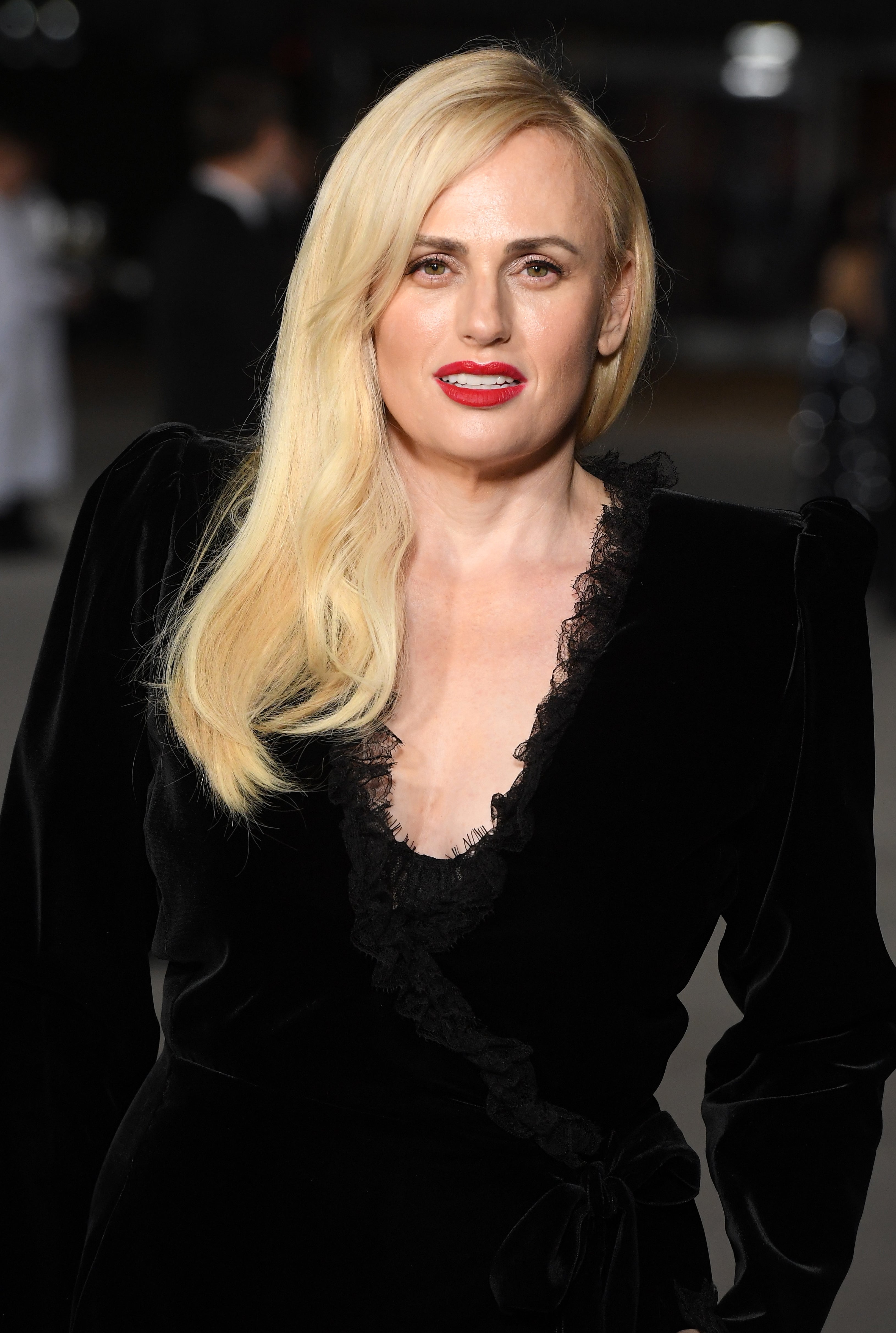 Rebel Wilson wearing a long-sleeved dress with lace trimming, posing at an event