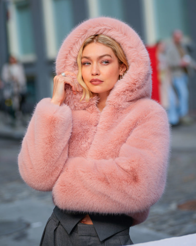 Gigi in a fluffy hooded jacket posing with her hand on her cheek