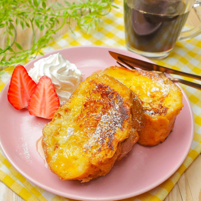 フレンチトーストとイチゴ、ホイップクリームが添えられた皿とカップのコーヒー。