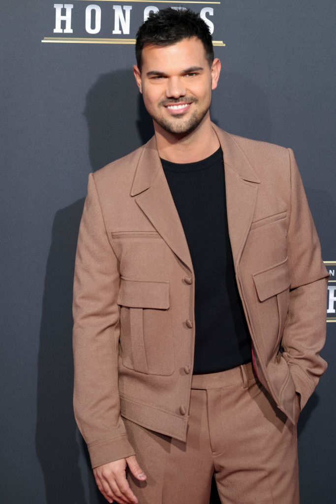 Taylor in a light suit with a dark shirt posing at an event