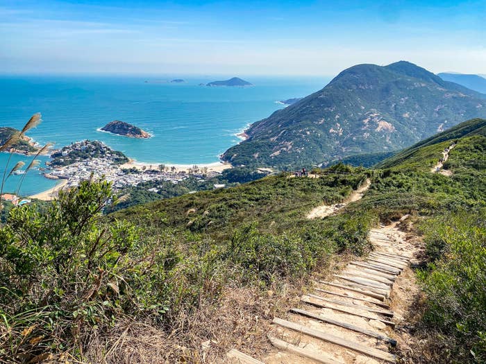 Scenic coastal view from a hill with a wooden trail leading down towards a village and beach