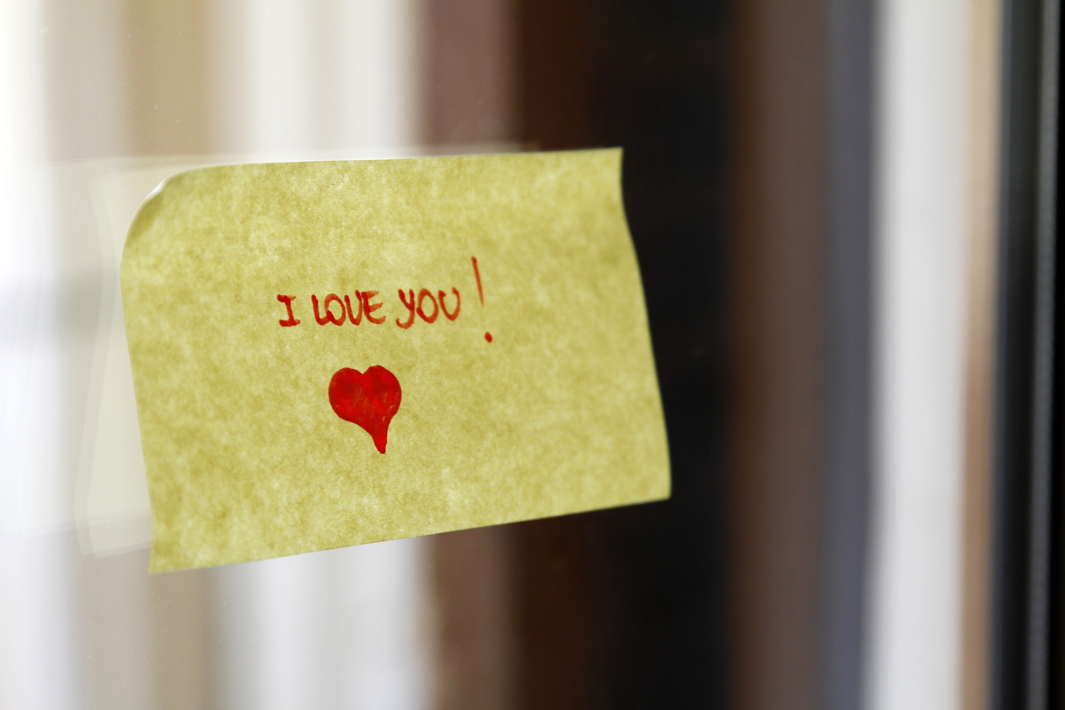 Sticky note on a surface with &quot;I love you!&quot; handwritten and a small heart drawn below the text