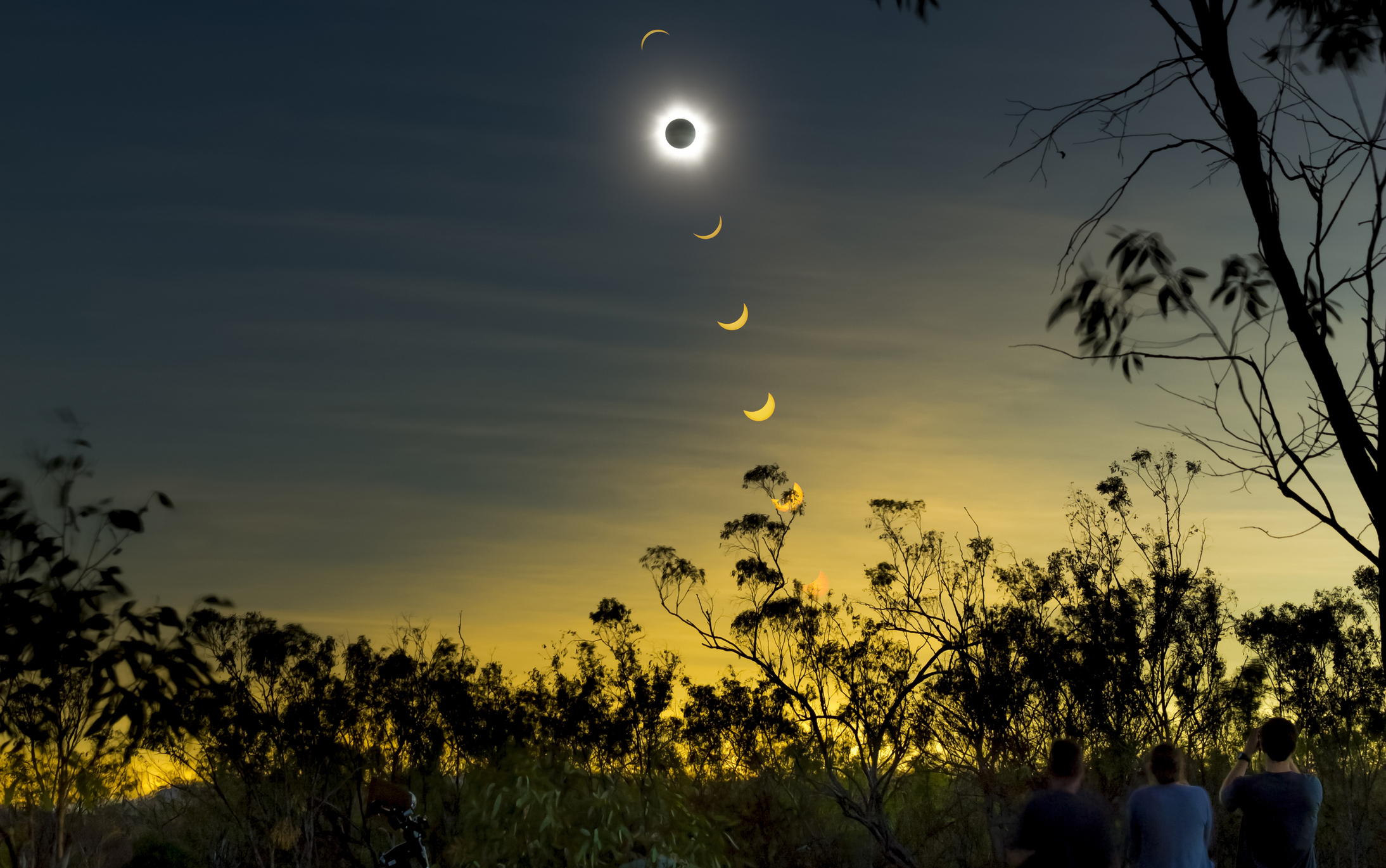Solar eclipse sequence over a silhouette of trees with onlookers