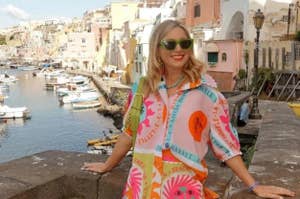 Woman in vibrant tropical print outfit with shorts and sunglasses, standing by a coastal backdrop for a style feature