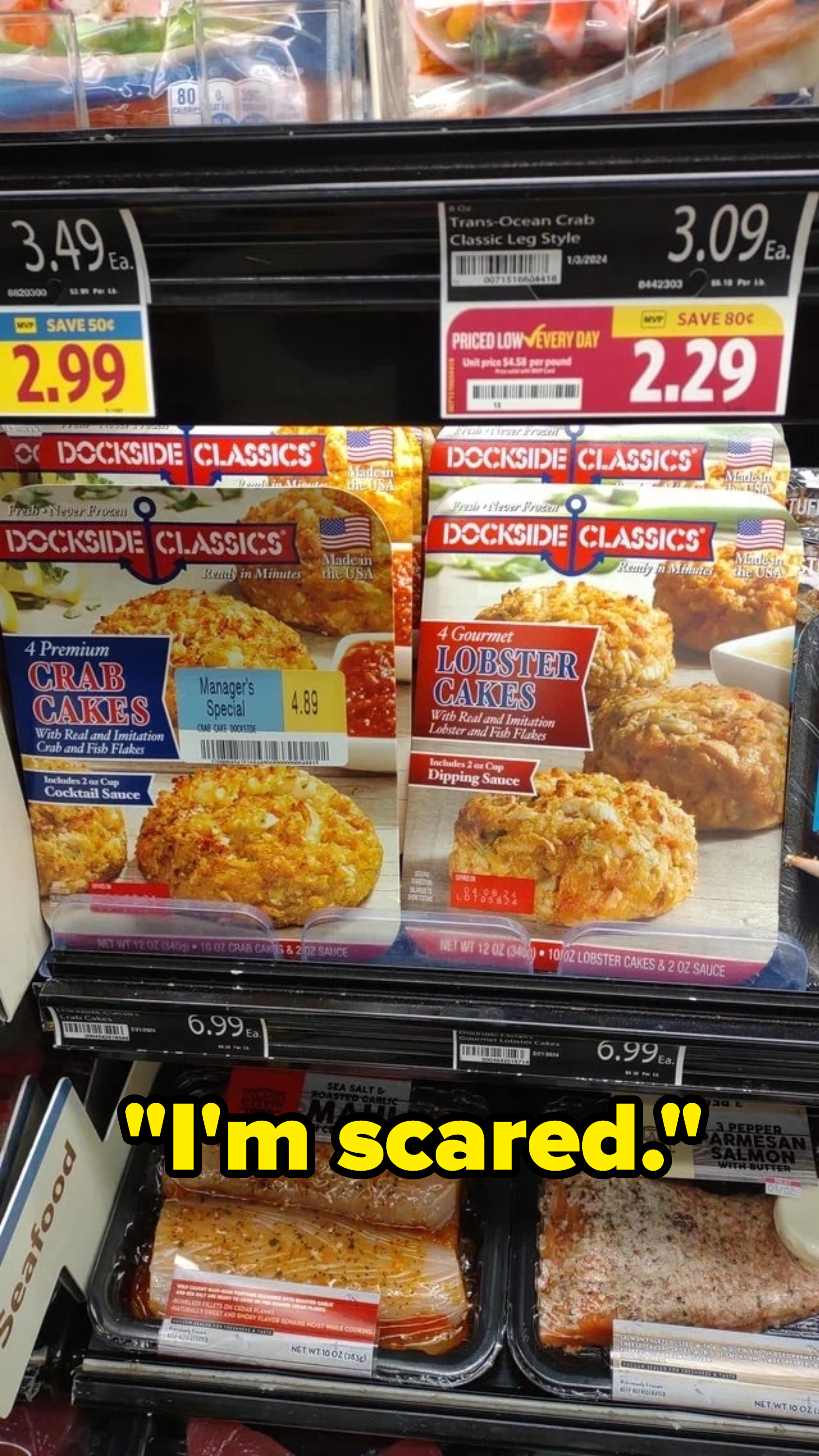 Supermarket freezer with various seafood options including crab cakes and lobster bisque. Prices and brand names visible