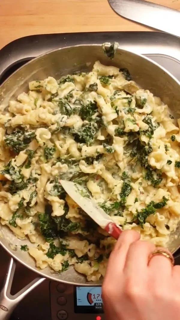 A person stirring creamy pasta with spinach in a pan on a stove