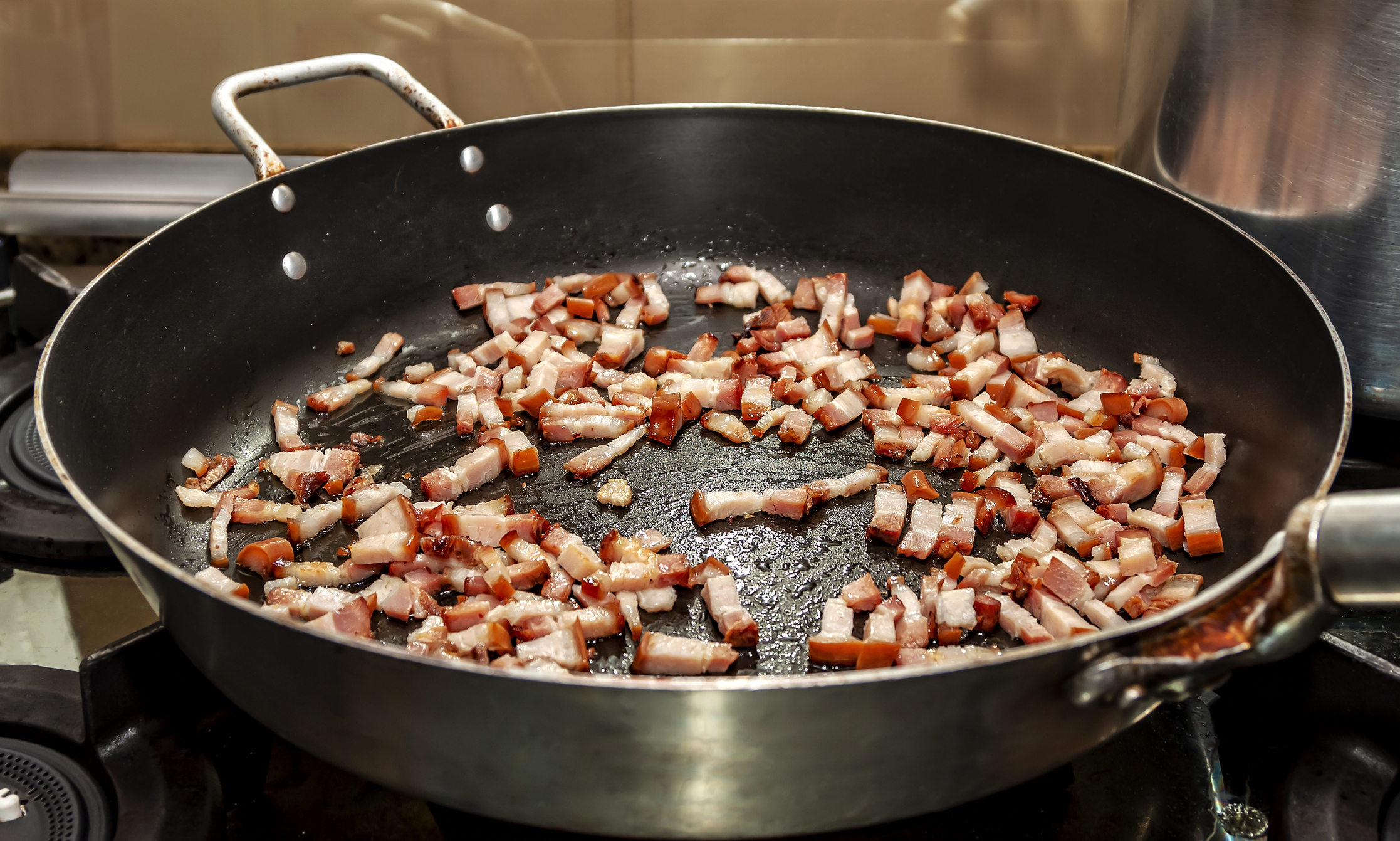 Bacon pieces sizzle in a frying pan on a stove