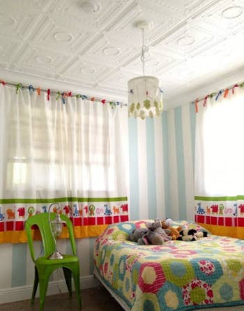 Children's bedroom with a patterned bedspread, stuffed toys on the bed, and colorful animal-themed curtains