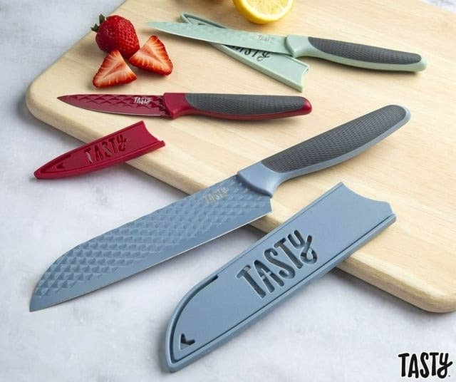 Four kitchen knives with protective blade guards on a cutting board with a strawberry