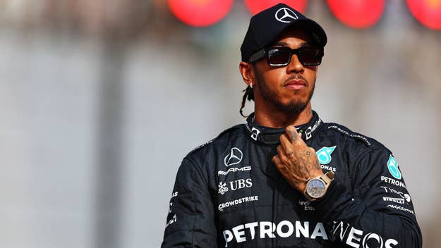 Lewis Hamilton in a racing suit with sponsor logos, hand over heart, standing solemnly
