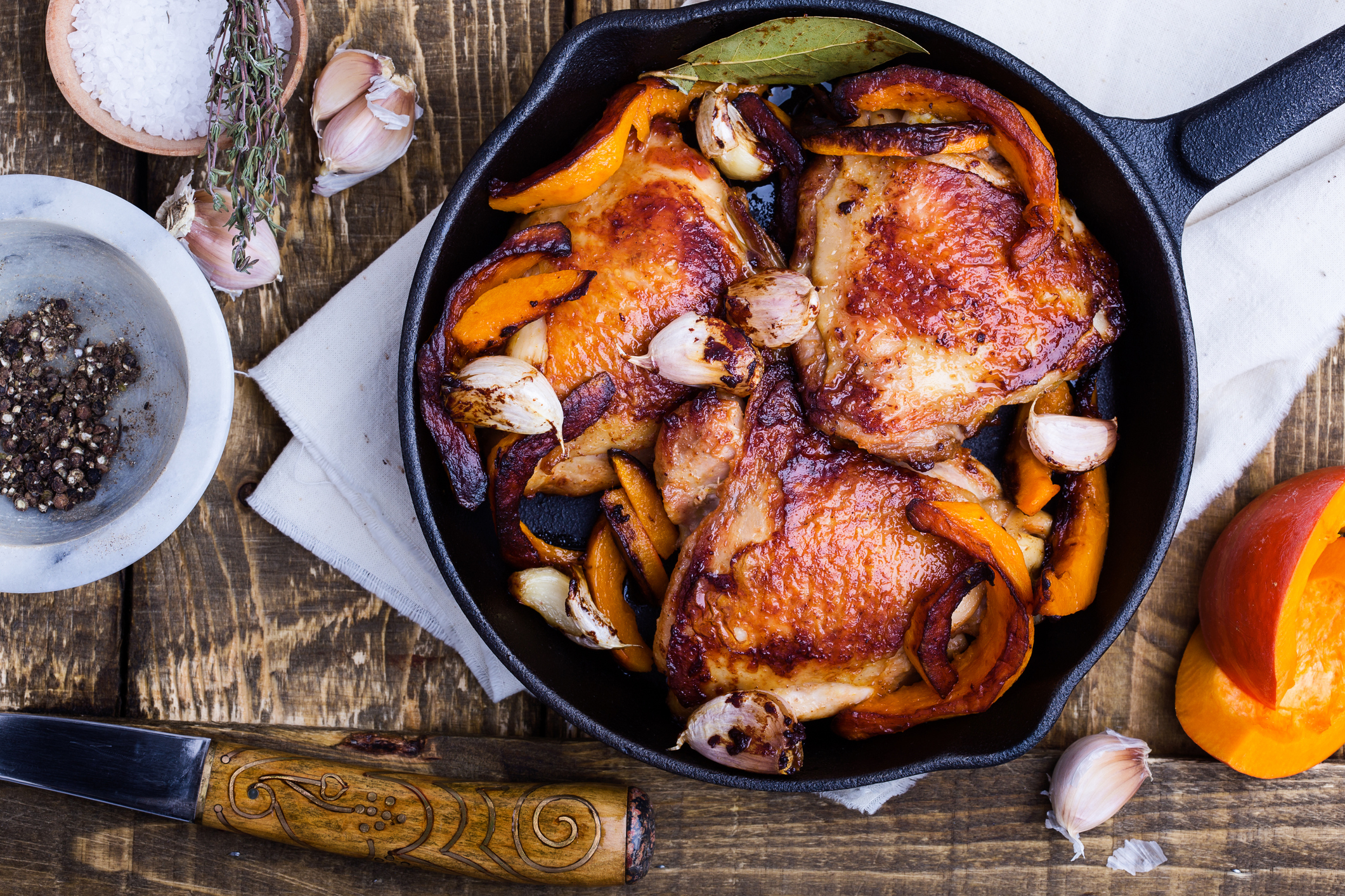 Skillet with roasted chicken thighs and vegetables on wooden surface