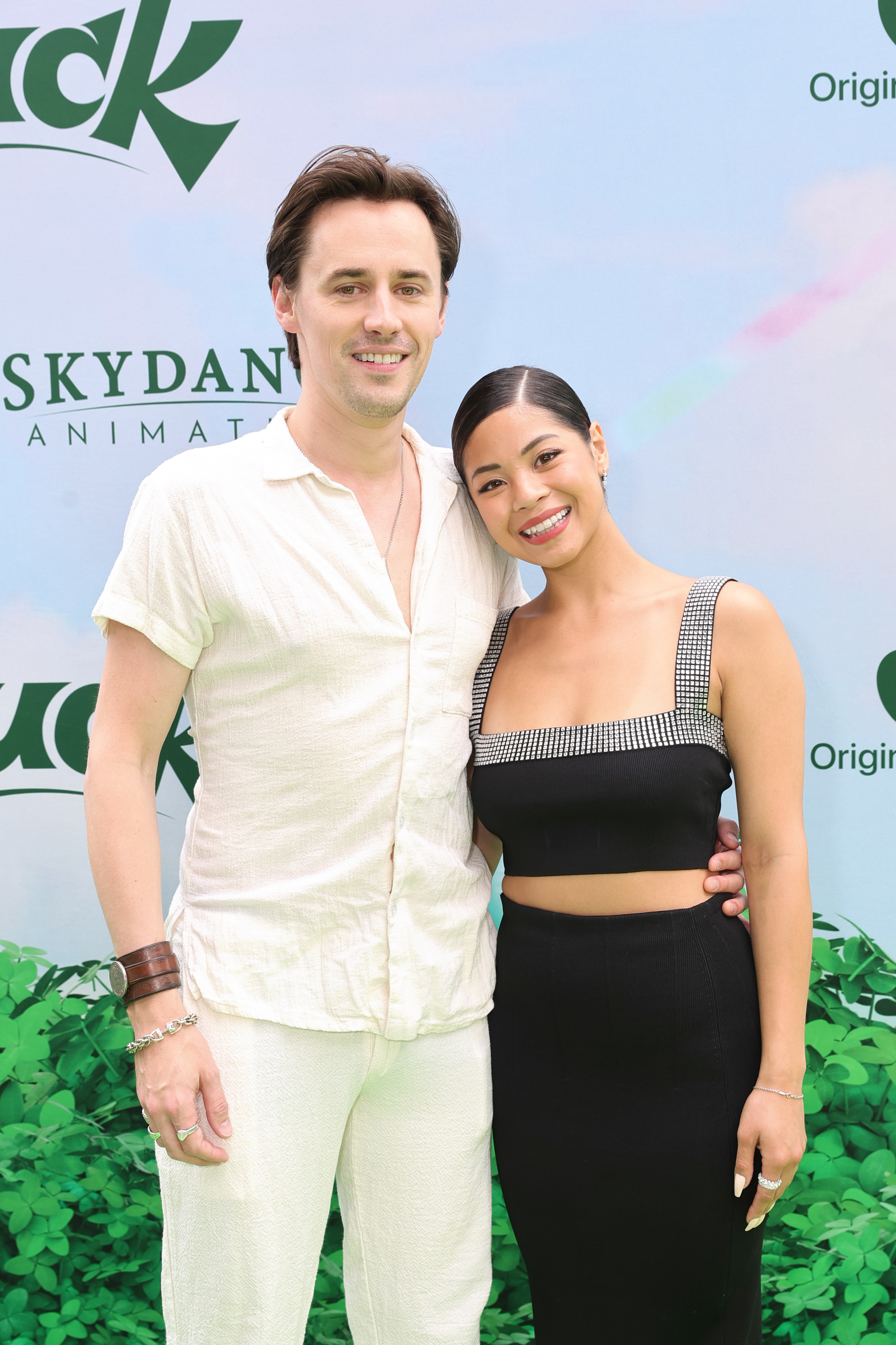 Two people posing, one in a casual white outfit, the other in a black top with a square neckline