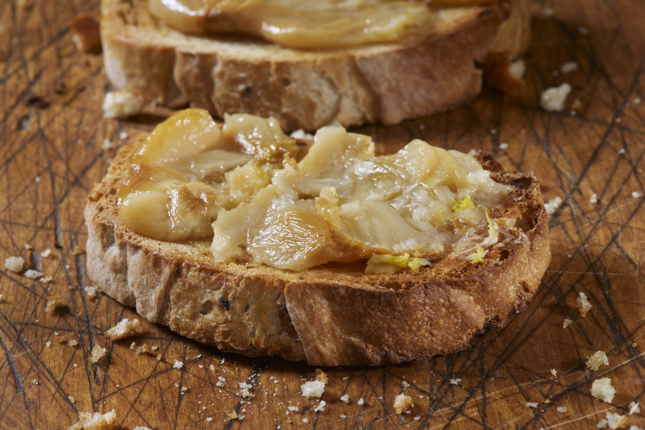 Two slices of toasted bread topped with melted cheese and onions on a wooden surface