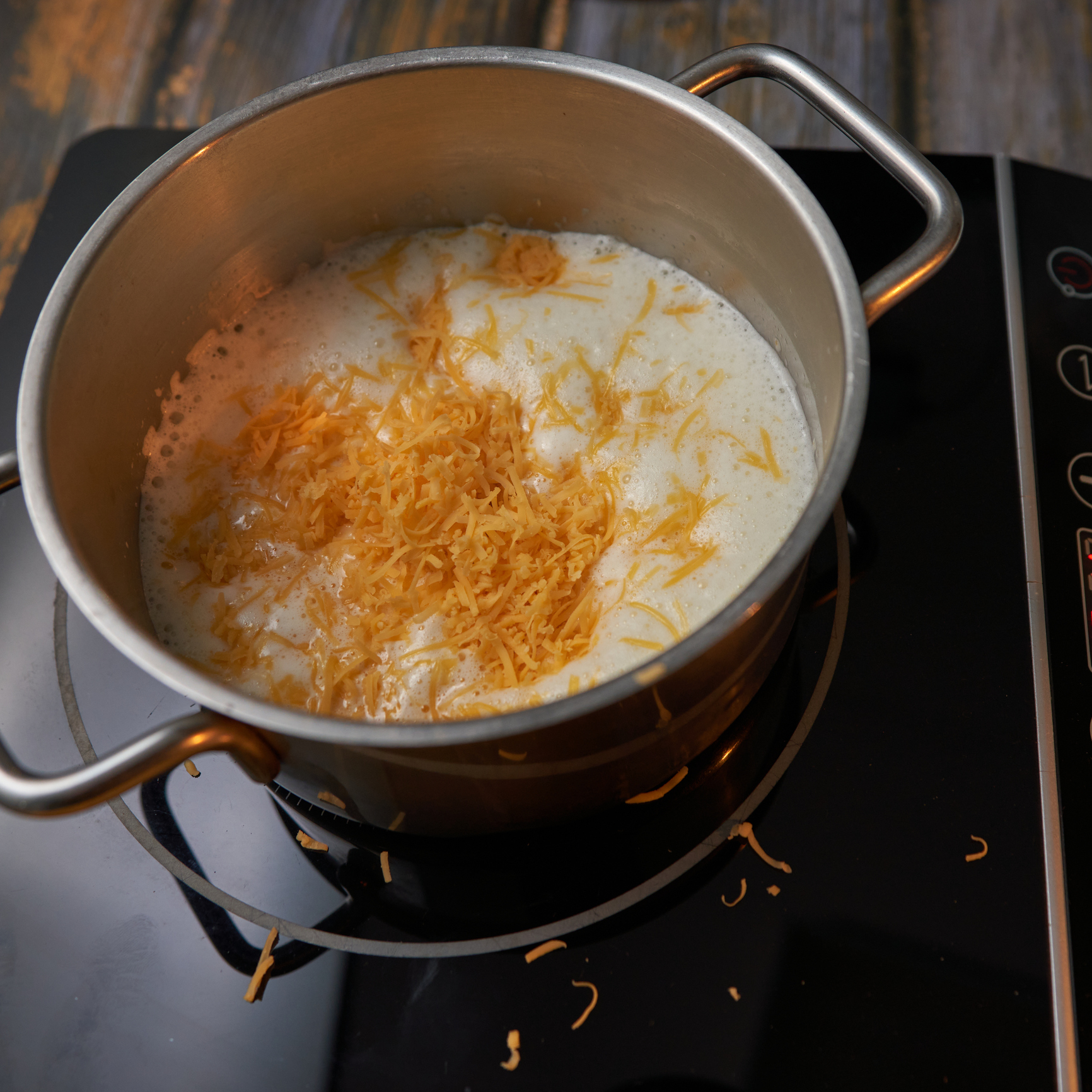 A pot on a stove with melting shredded cheese in a white liquid