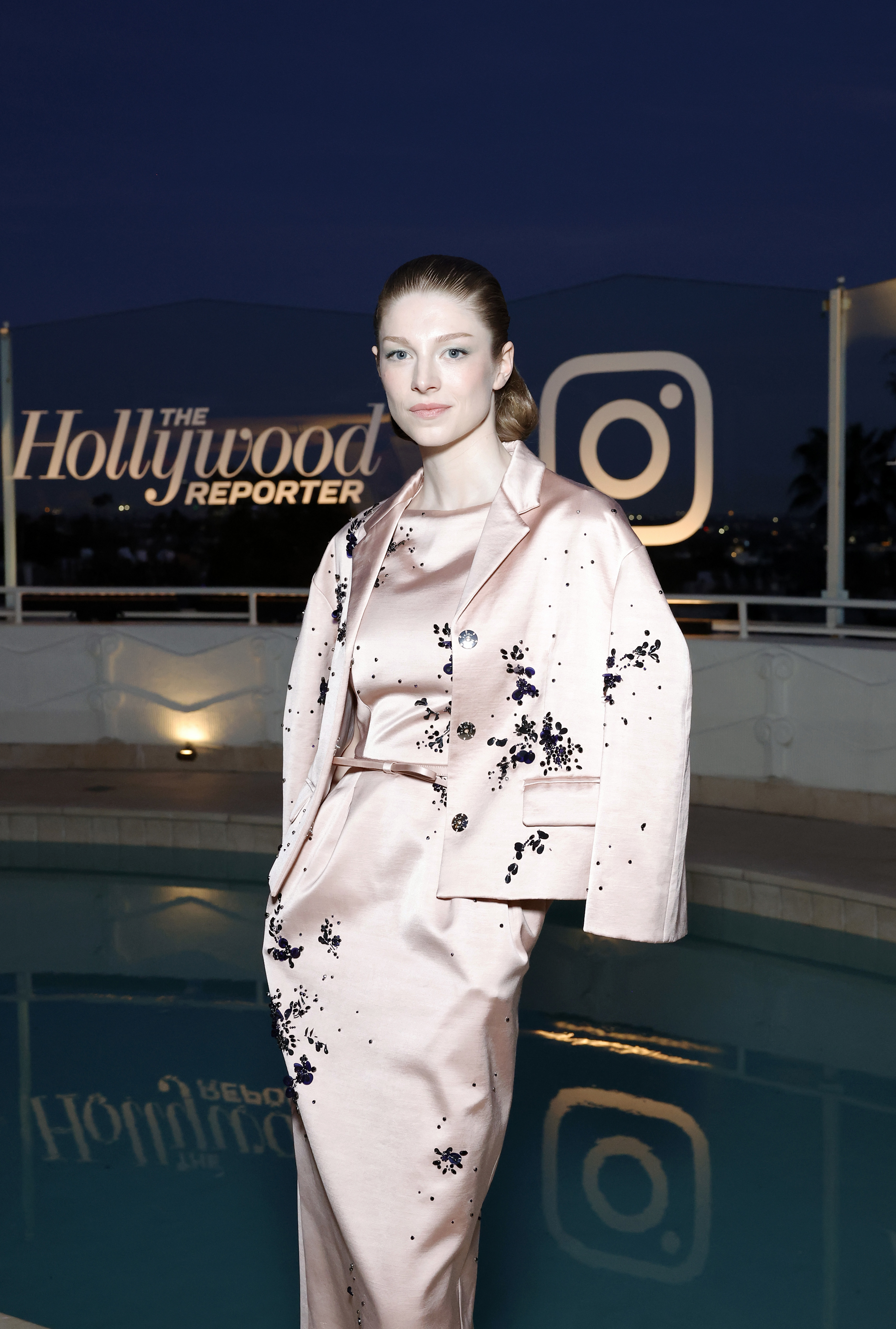 Woman in elegant pink suit with black detailing, posing by a pool at a Hollywood Reporter event