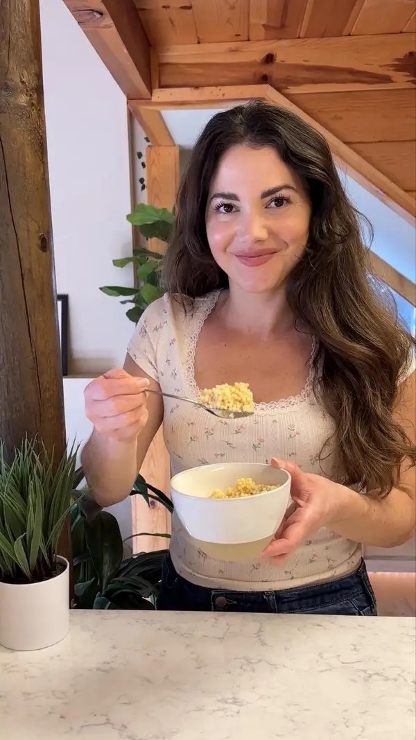 Woman smiling at camera holding a bowl of rice, in a kitchen setting