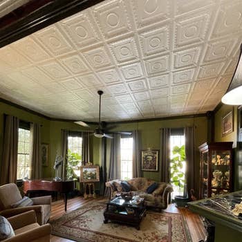 A vintage-style living room with ornate ceiling tiles, antique furniture, and a patterned area rug