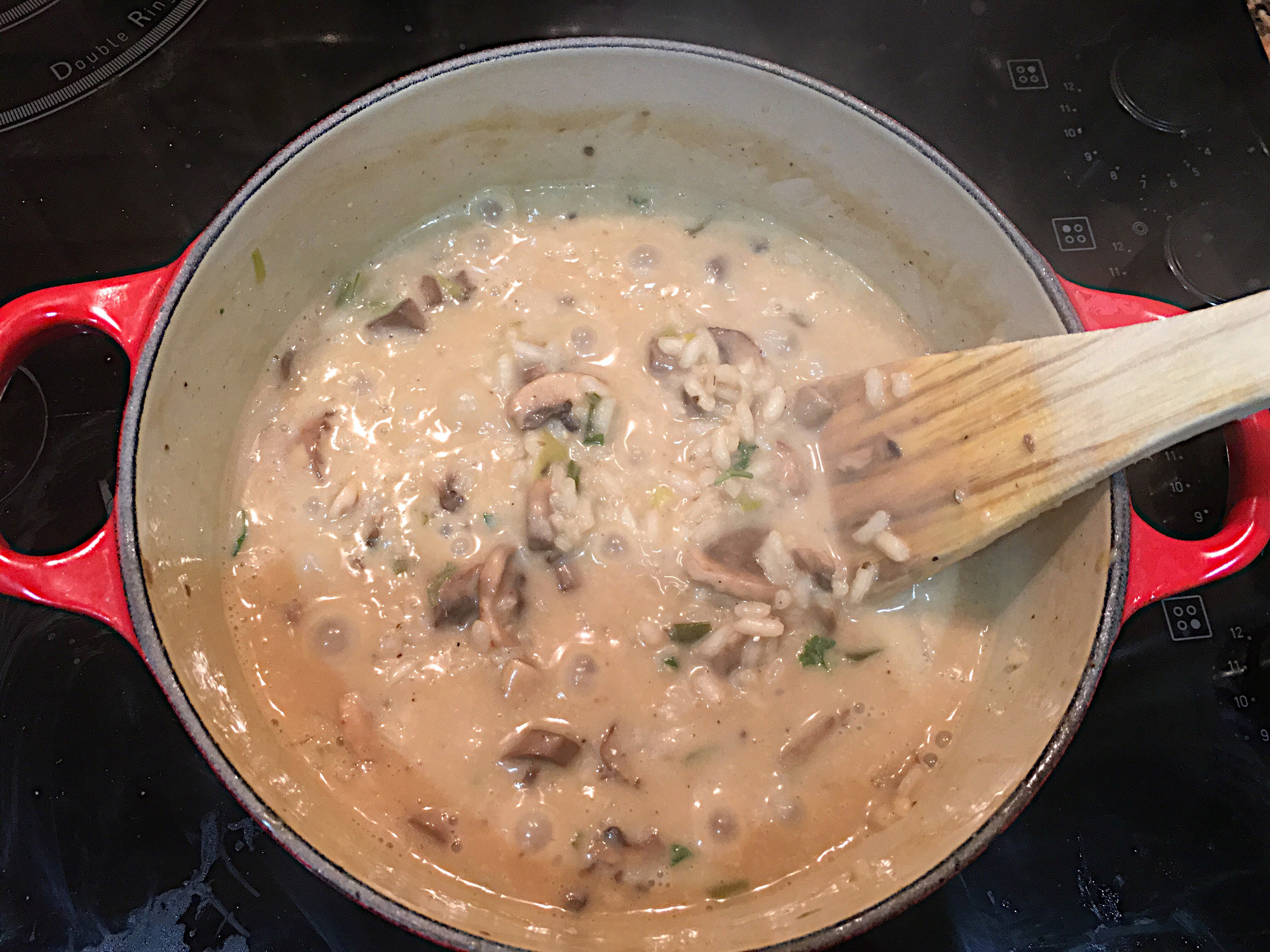 A pot of creamy mushroom risotto being stirred with a wooden spatula