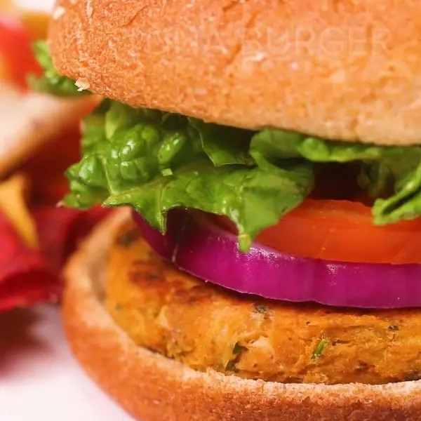 Close-up of a veggie burger with lettuce, tomato, and onion on a bun, with chips on the side