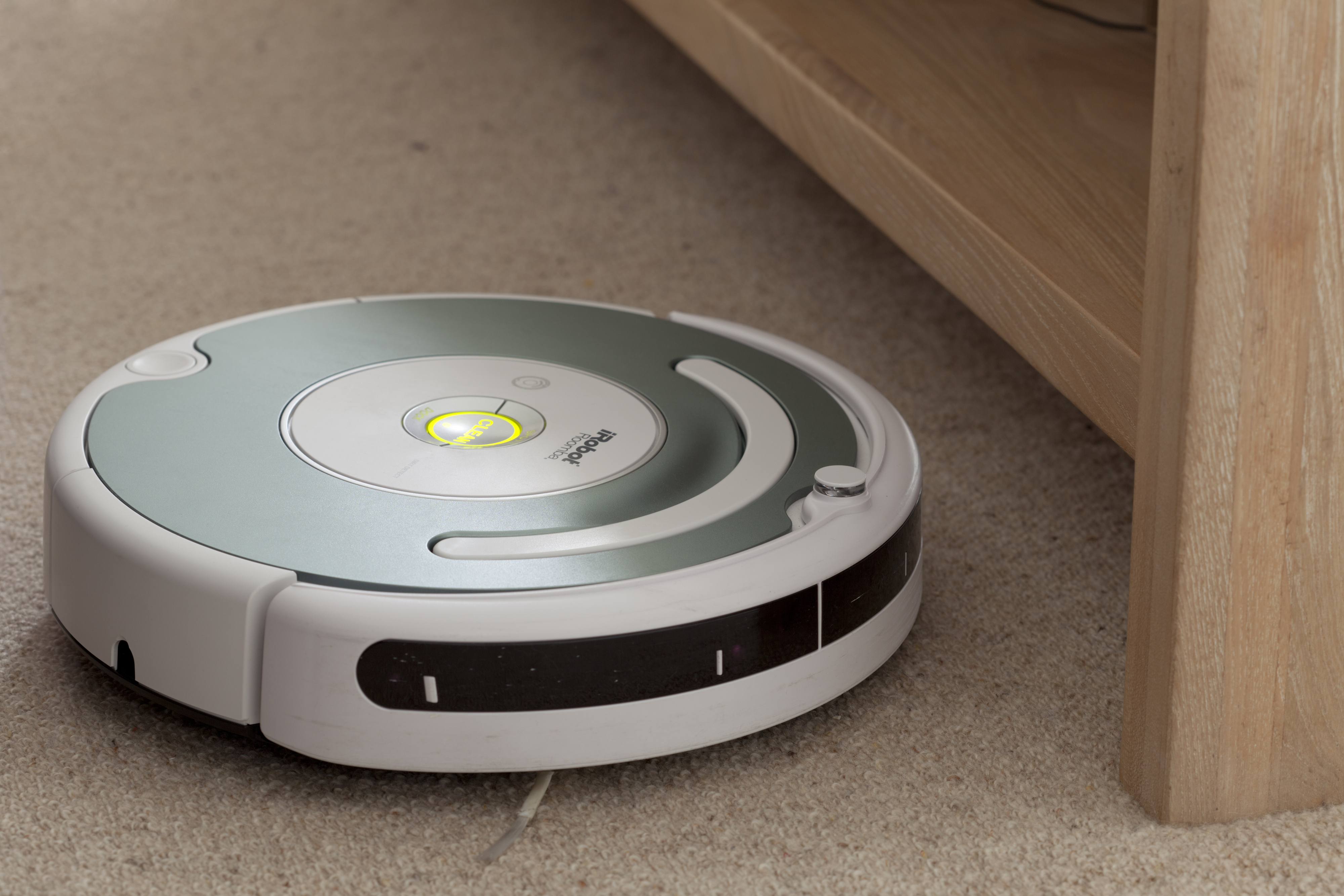 Robotic vacuum cleaner operating on a carpet near a piece of furniture