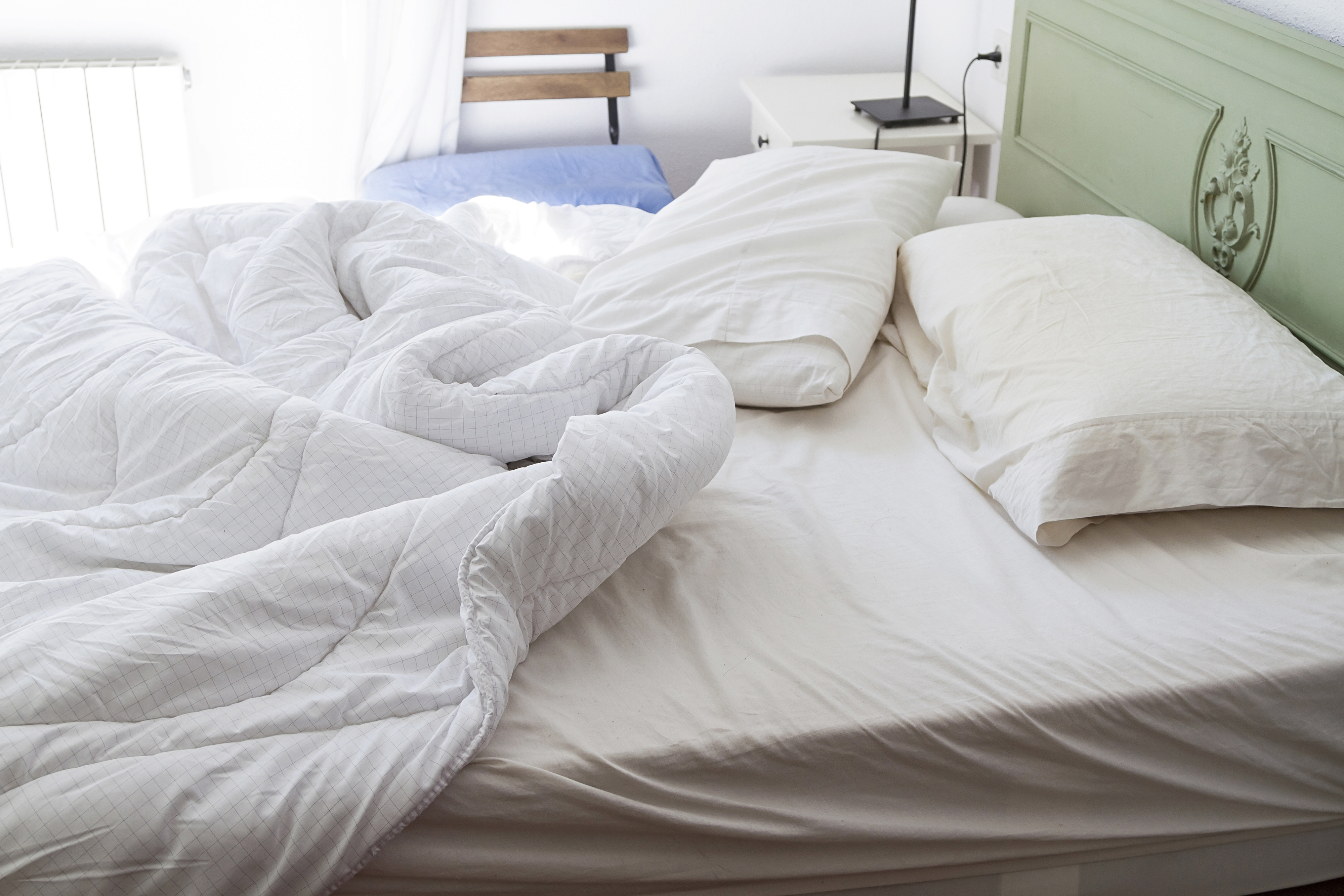 Unmade bed with a rumpled white duvet and two pillows in a bright room