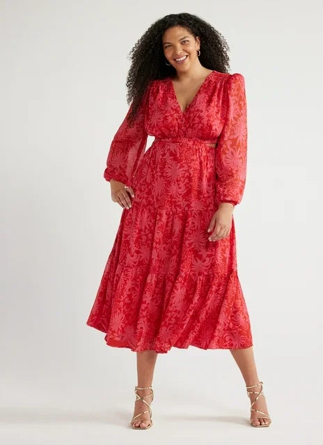 model in patterned red midi dress with long sleeves and V-neckline, standing with hands on hips
