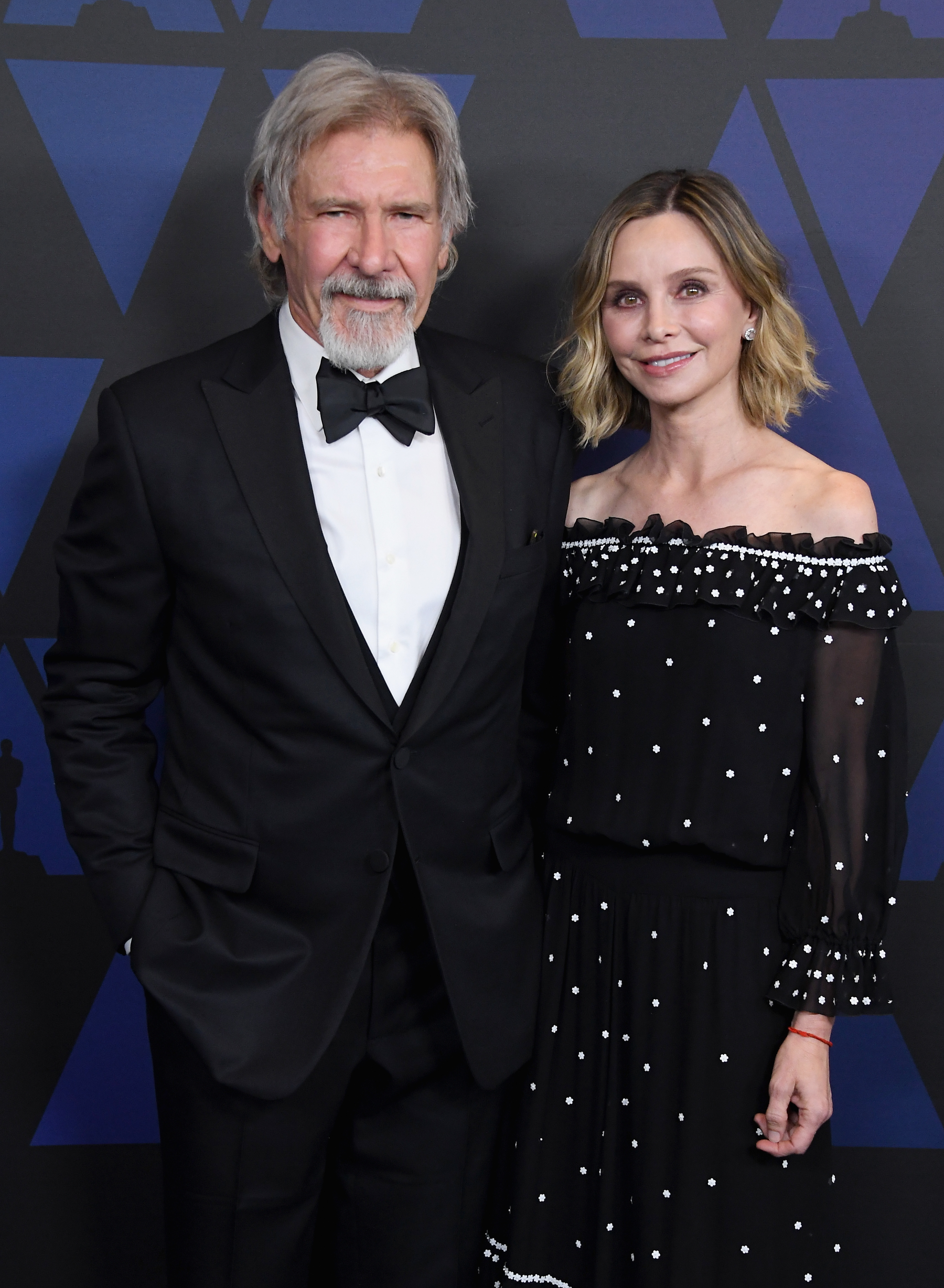Two celebrities in formal wear, man in a tuxedo and woman in a polka-dot dress with sheer details