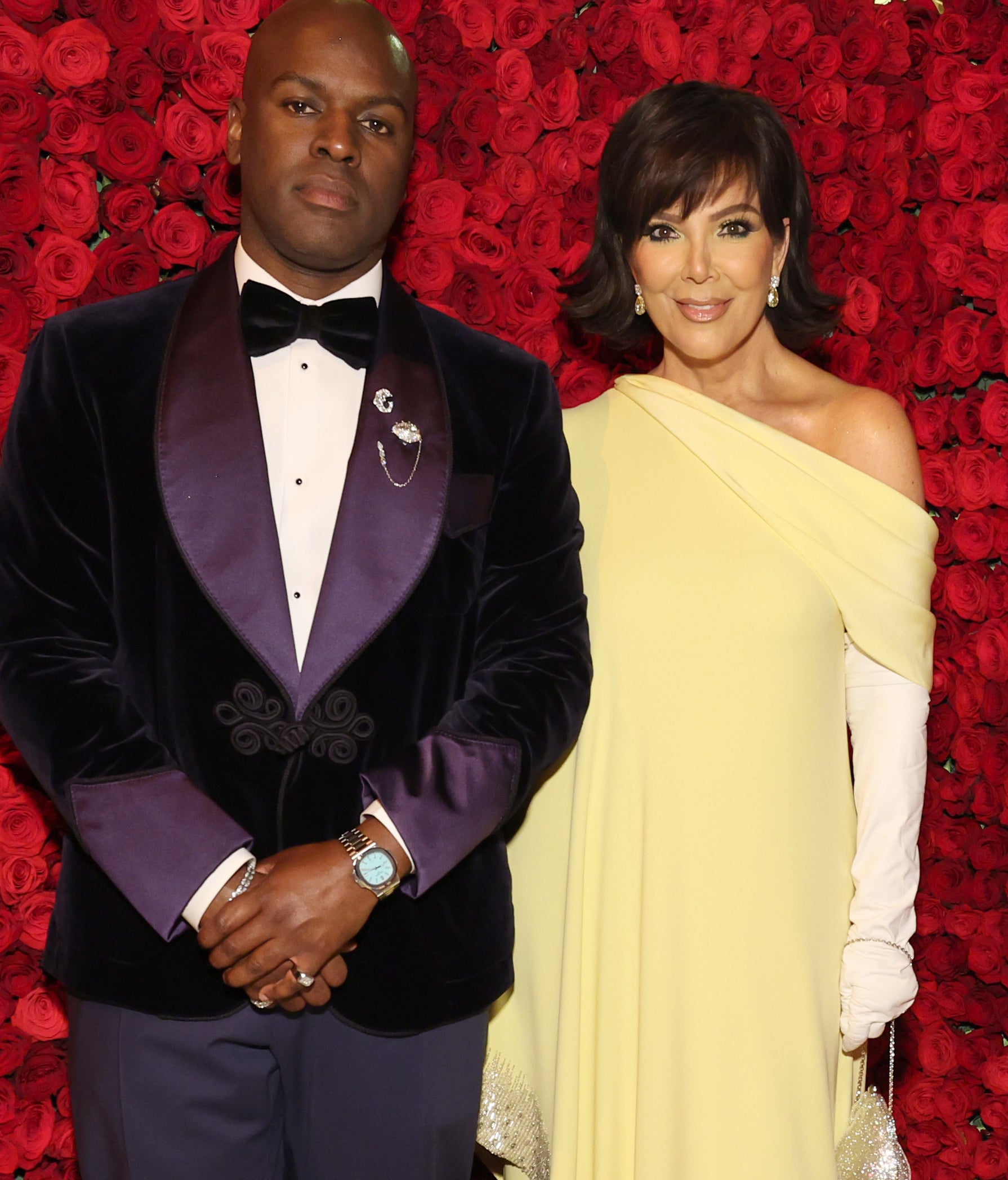 Two celebrities pose together; one in a velvet tuxedo and the other in a one-shoulder gown