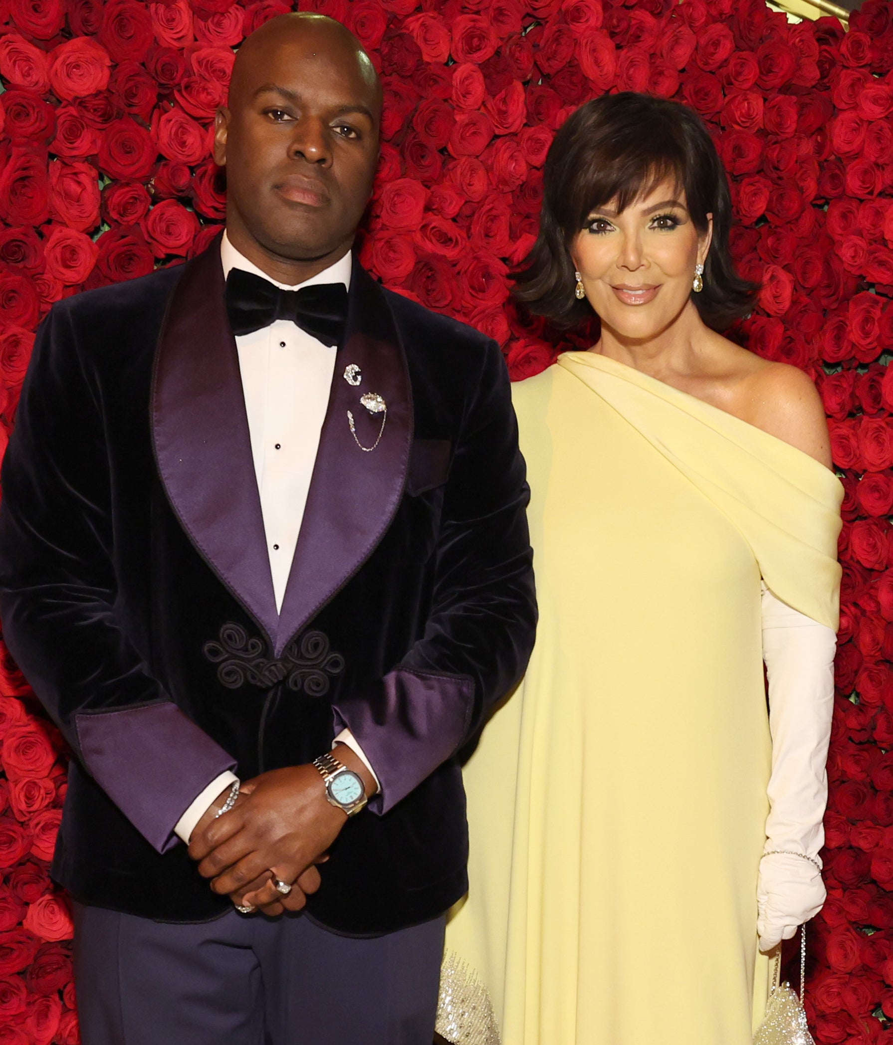 Two celebrities pose together; one in a velvet tuxedo and the other in a one-shoulder gown