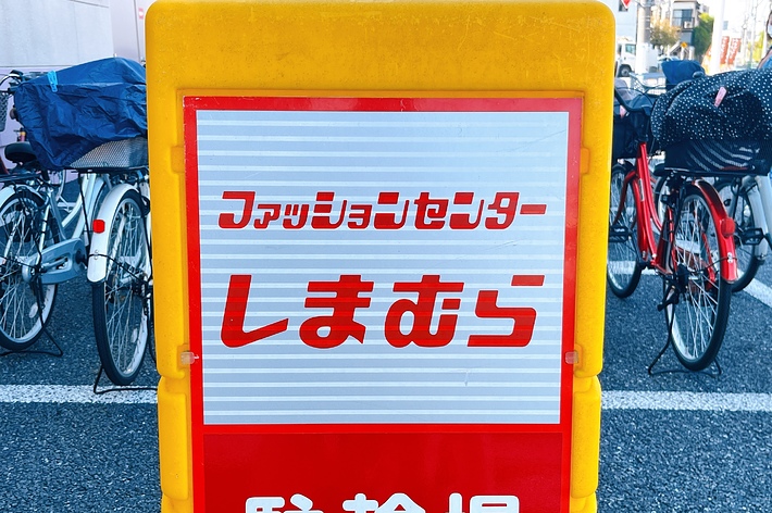 Signboard in Japanese with bicycles parked in the background. Text content summarized: &ldquo;Folding bicycles parking area.&quot;