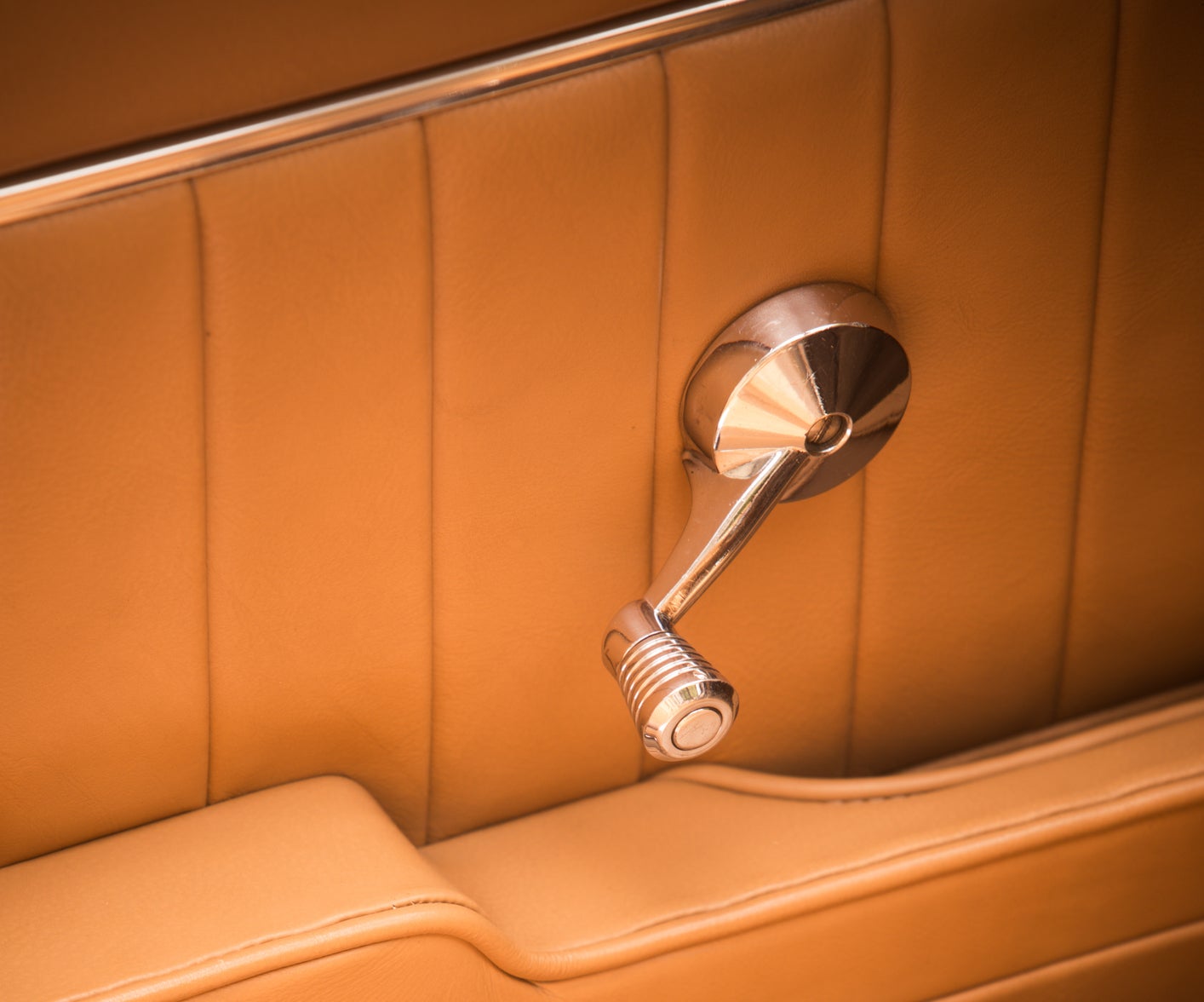 Vintage car&#x27;s interior showing a chrome door handle and leather upholstery