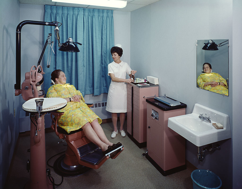 A vintage dental office scene with a patient in a chair, a dentist standing by, and a mirrored reflection of the patient