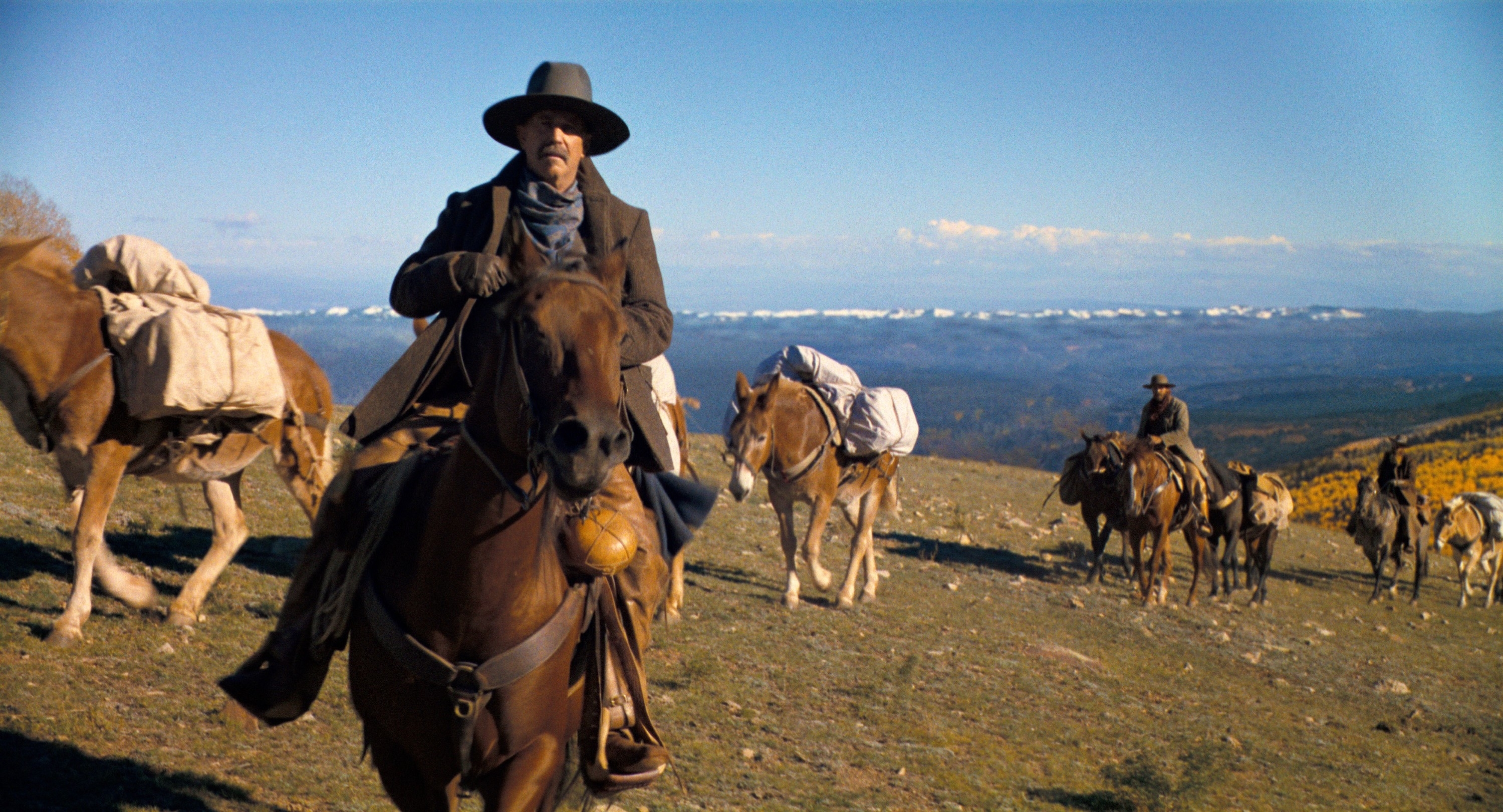 Kevinon horseback with traditional Western attire leading a pack train in a mountainous landscape