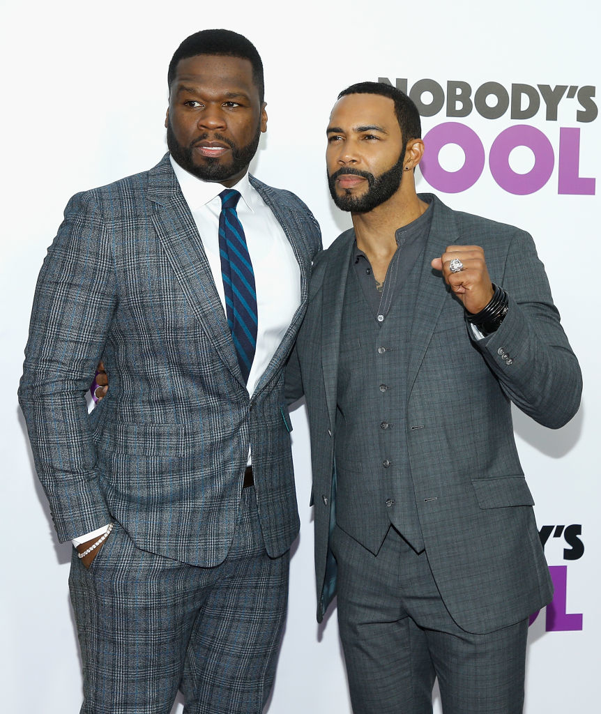 50 Cent and Omari Hardwick pose together, both dressed in suits at an event