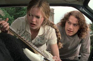 Kat from 10 Things I Hate About You holding a guitar in the back of a car while Patrick looks on and smiles