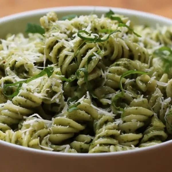A bowl of pesto pasta garnished with cheese and herbs