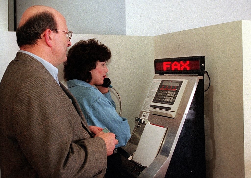 Two individuals using a fax machine, capturing a moment of past office technology